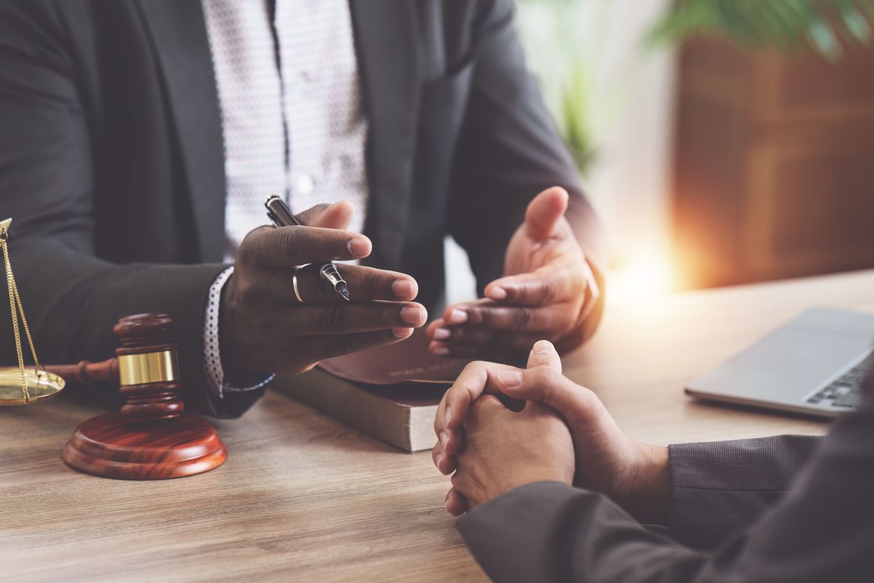 A man in a suit is sitting at a table talking to another man.