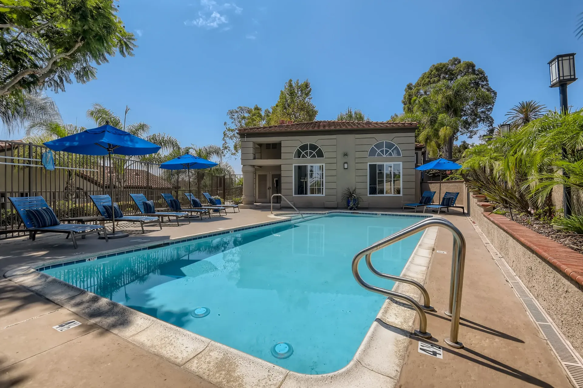 Outdoor pool area with blue umbrellas and lounge chairs at a residential community.