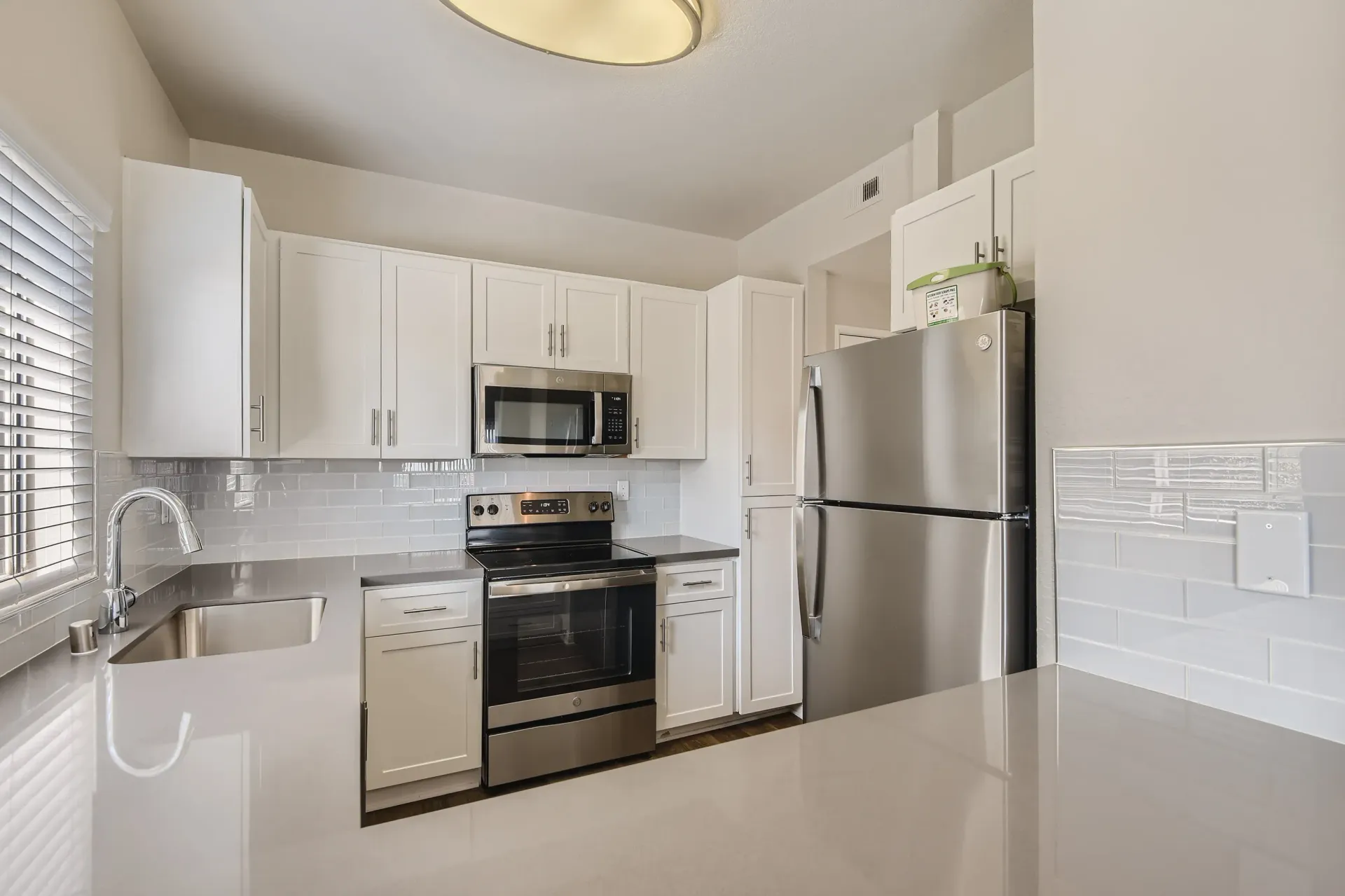 Modern white kitchen with stainless steel fridge, stove, microwave, and sink.