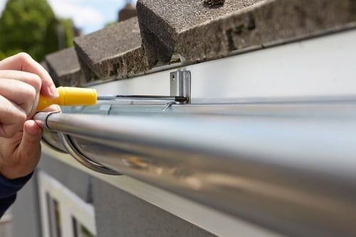 A person is fixing a gutter with a screwdriver.