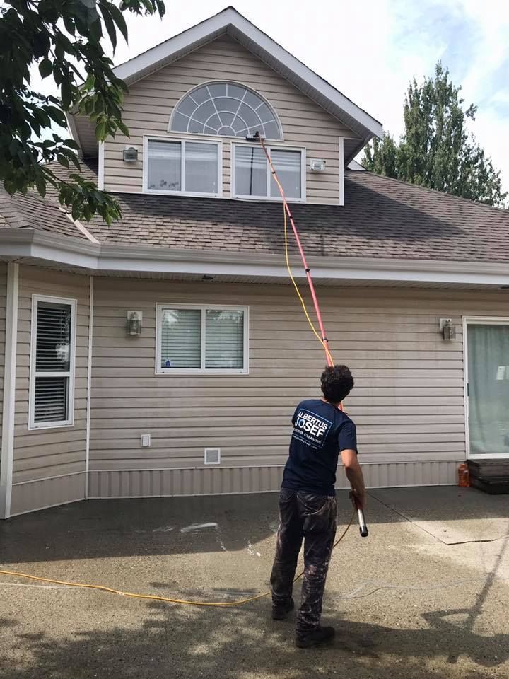 A man is cleaning the windows of a house with a hose.
