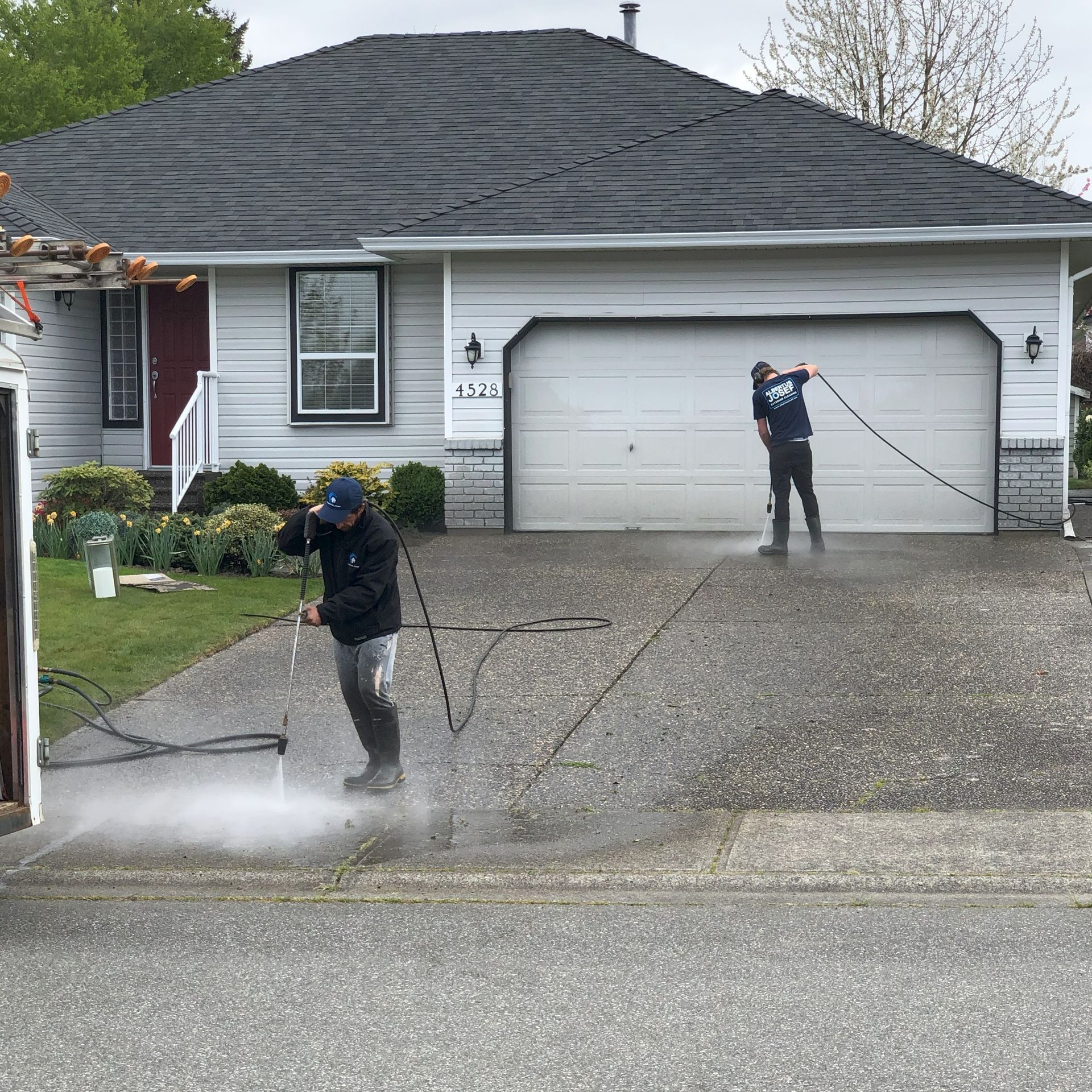 Two men are cleaning a driveway in front of a house