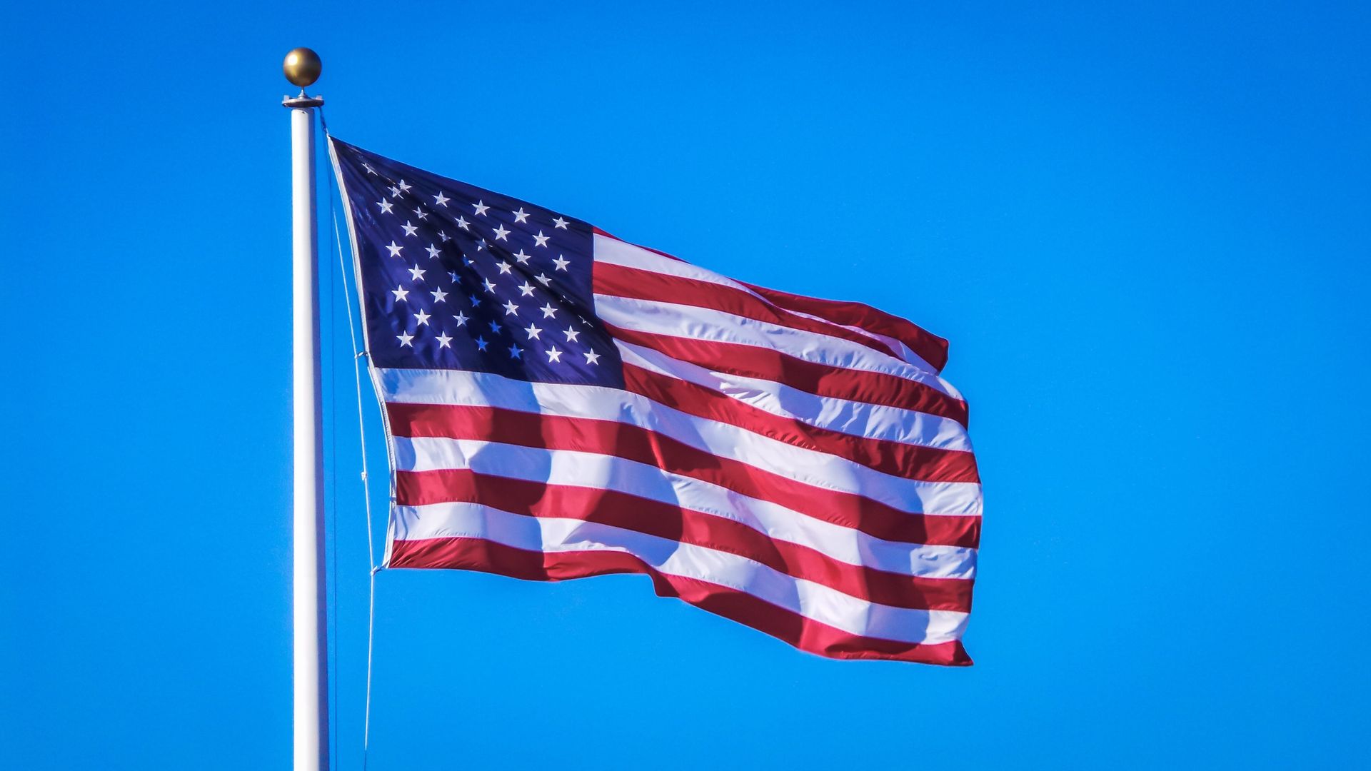 American flag waving on a flagpole against a clear blue sky