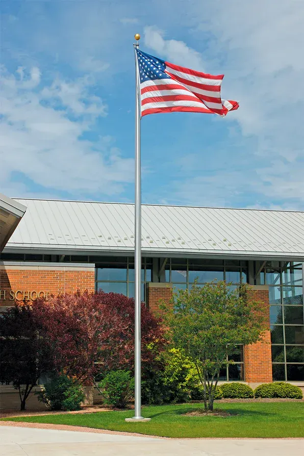 American flag flying on a pole outside a brick and glass building on a landscaped lawn