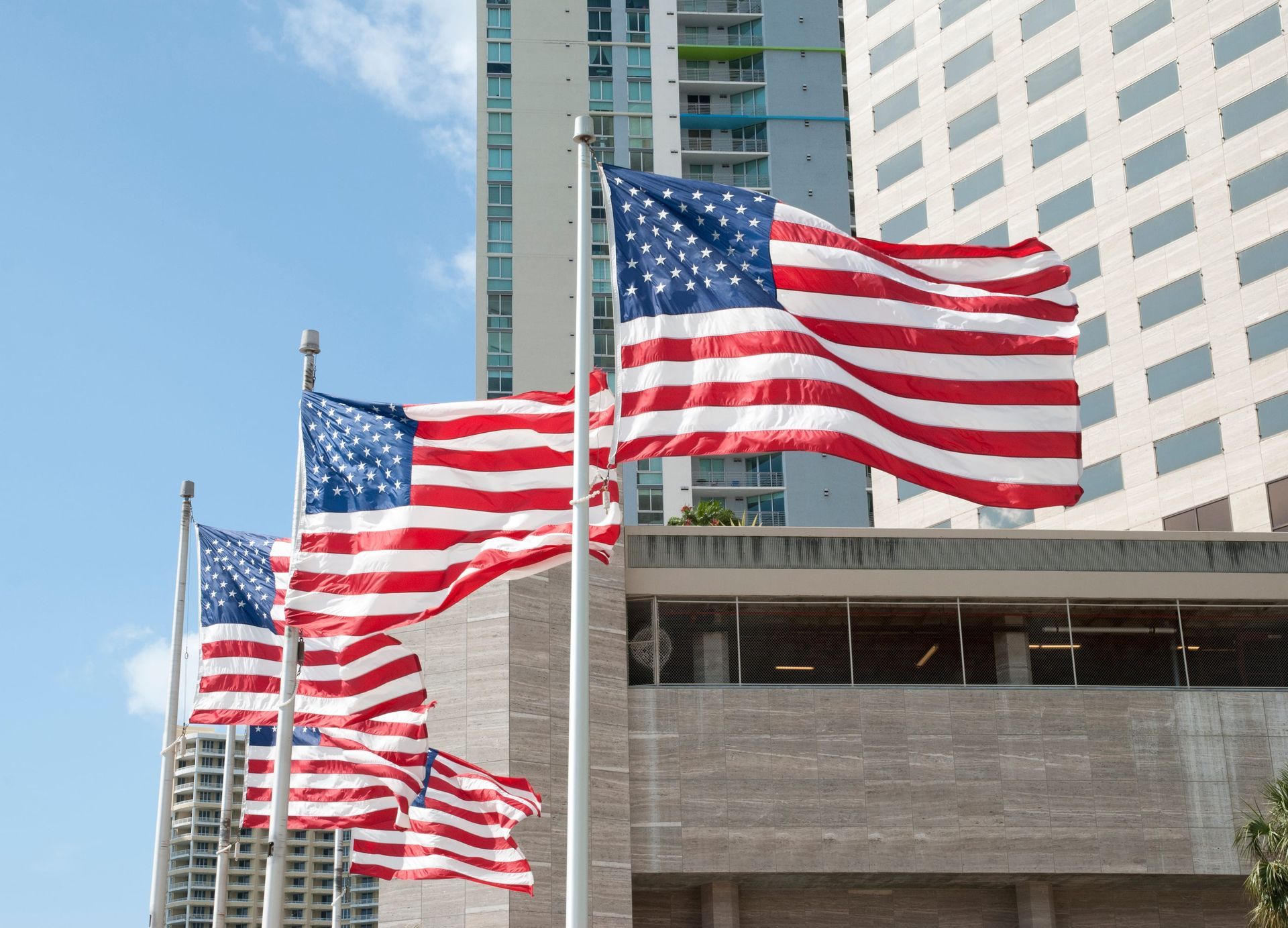 Several U.S. flags waving in front of a city building under a blue sky