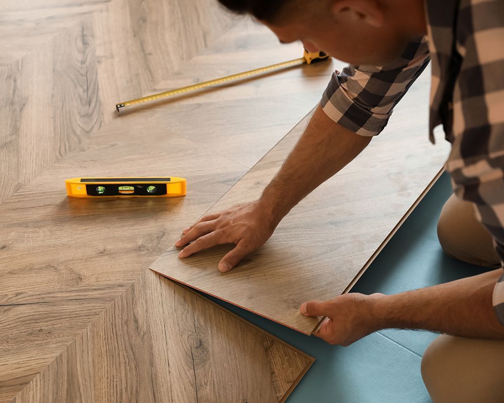 A man is installing a wooden floor with a level and tape measure.