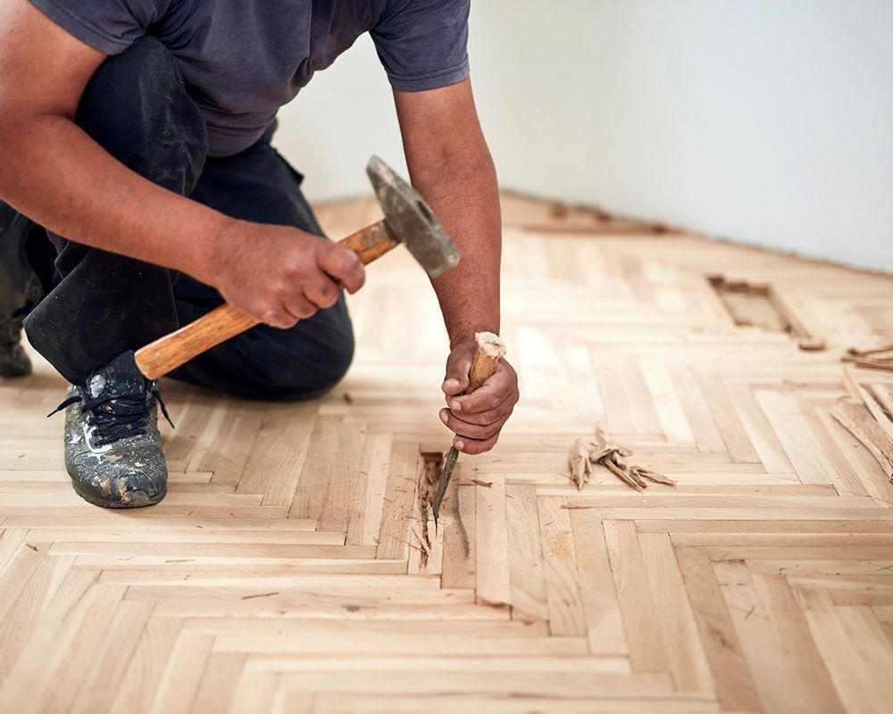 A man is kneeling down and using a hammer to fix a wooden floor.