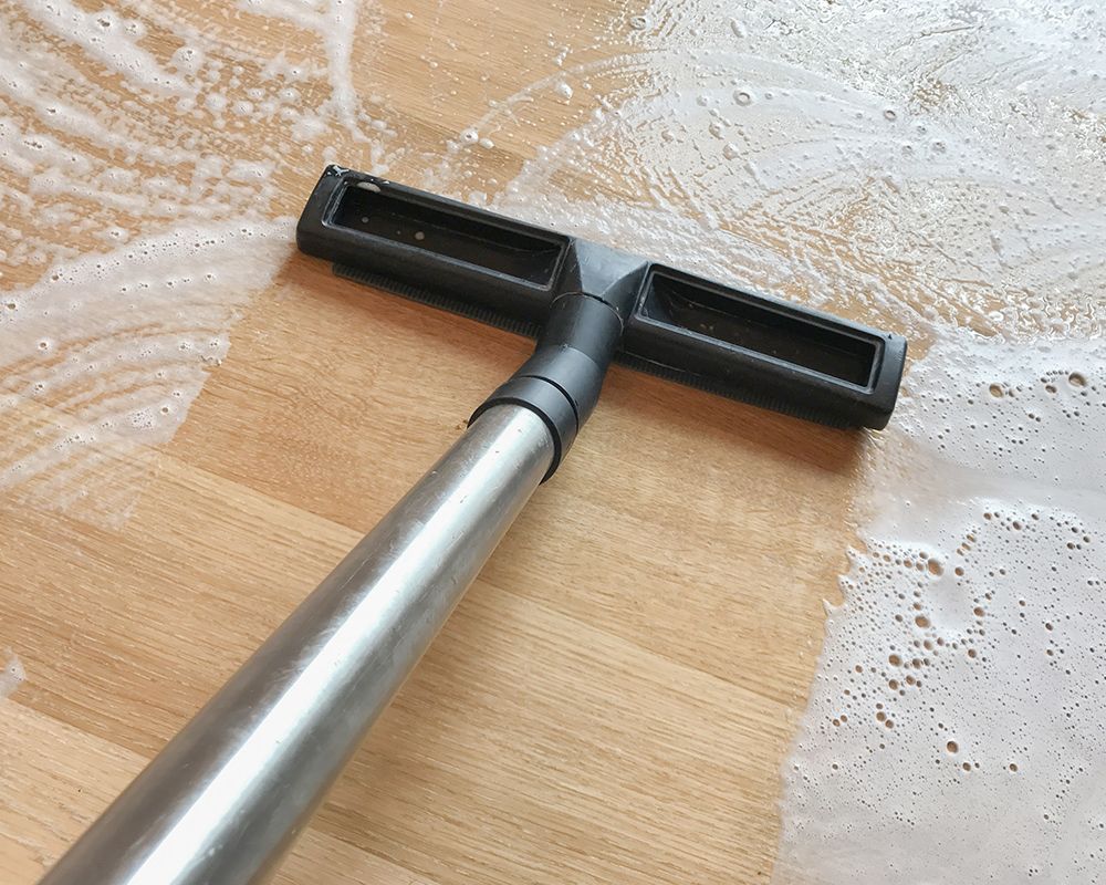A vacuum cleaner is cleaning a wooden floor with foam.