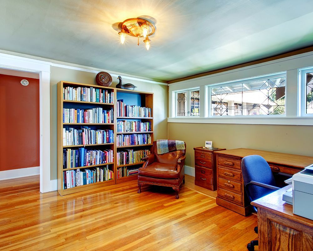 A living room with hardwood floors , a chair , a desk , and a bookshelf filled with books.