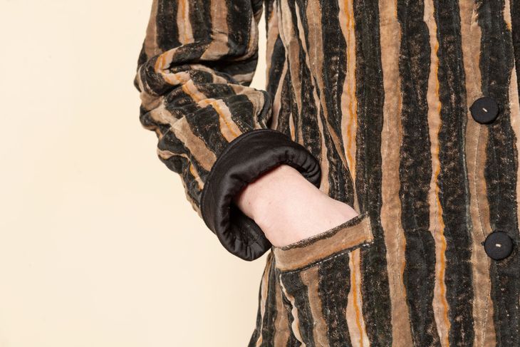 Braccio in cappotto a righe marrone e nero con polsino scuro.