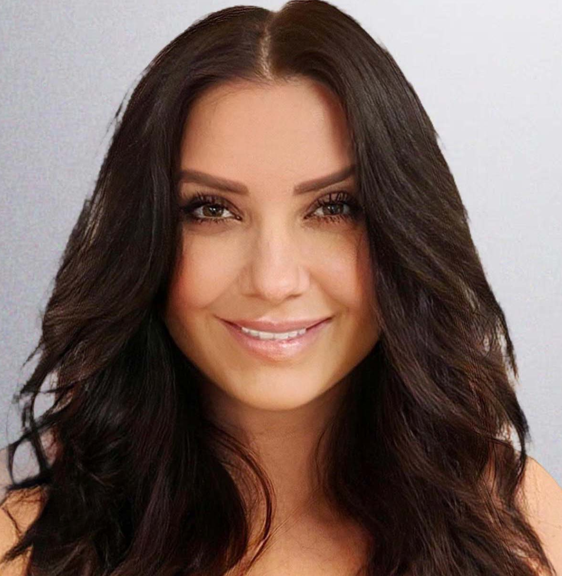 Woman with dark wavy hair smiles at the camera, neutral background.