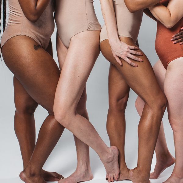 Four pairs of legs in nude-colored bodysuits stand close together, varying skin tones.