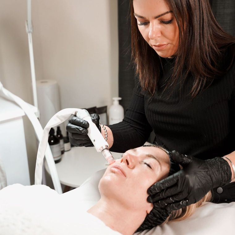 Woman performing a facial procedure on another woman, both wearing black gloves. hifu melbourne