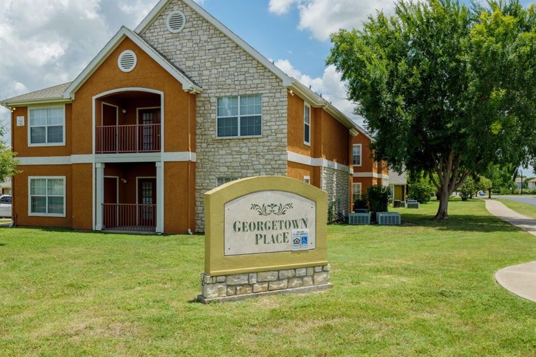 Apartment building with stone facade and sign reading “Glenbrook Plus” on a grassy lawn