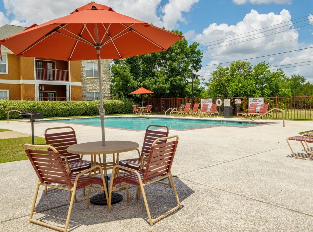 Outdoor pool area with orange umbrellas, patio tables, and chairs beside an apartment building.