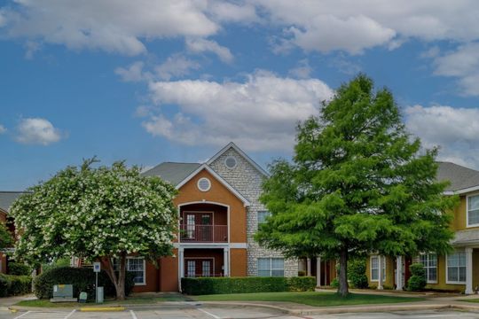 Suburban apartment buildings with trees and a partly cloudy blue sky