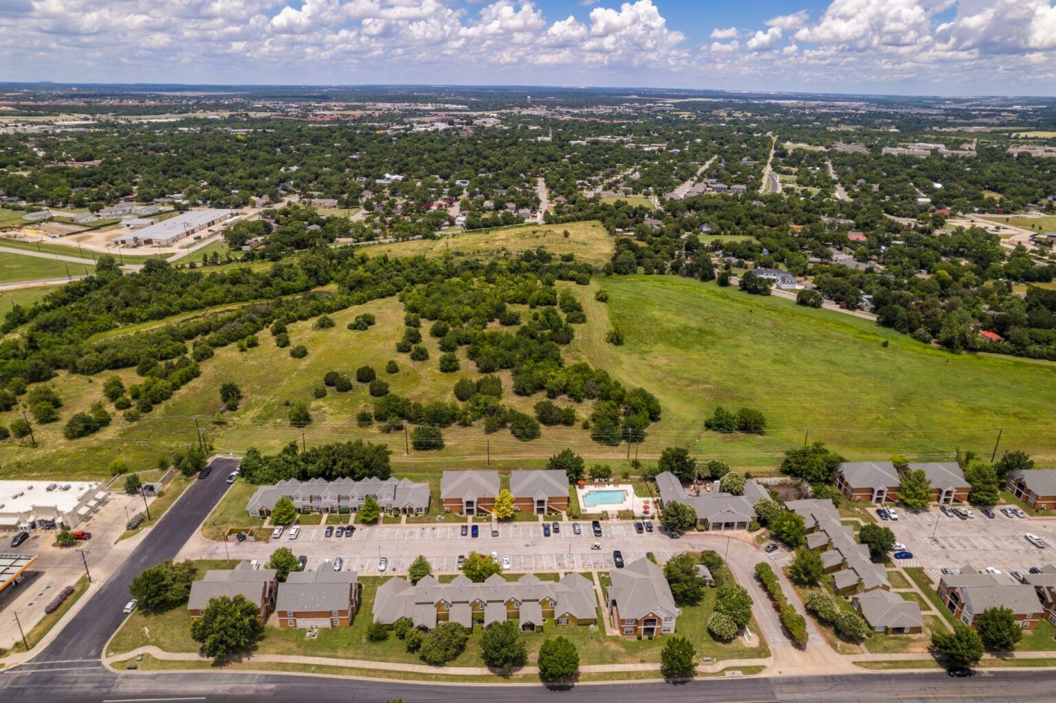 Aerial view of suburban neighborhood beside a large green field under a partly cloudy sky
