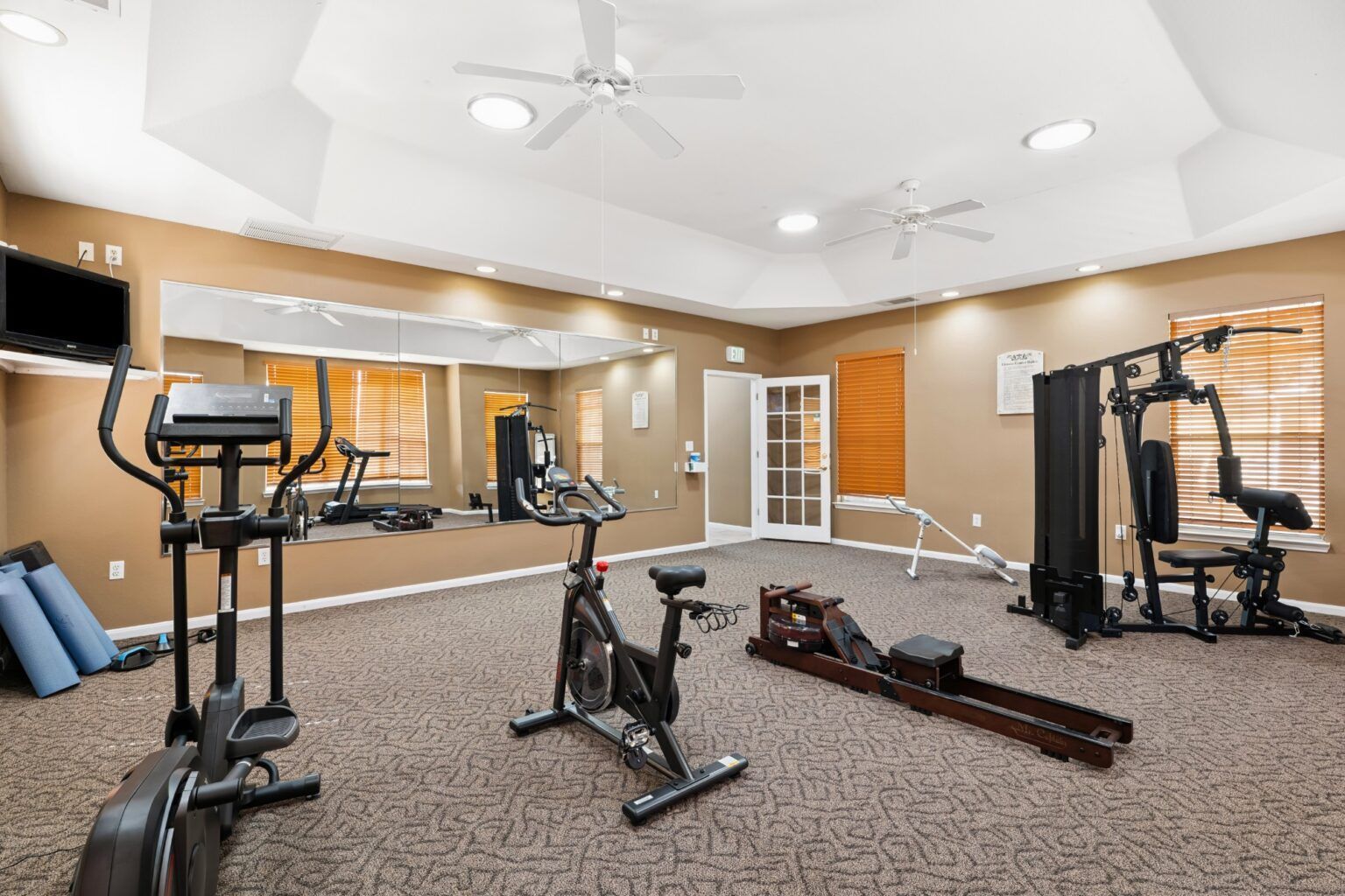 Gym room with cardio machines, weight equipment, and mirrors on beige carpet