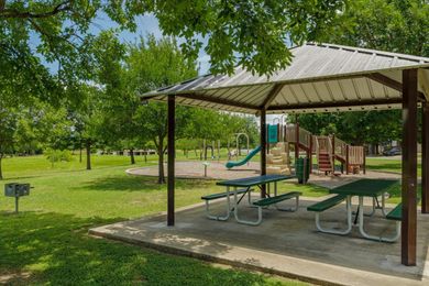 Park pavilion with picnic tables, playground, and green trees in a grassy park