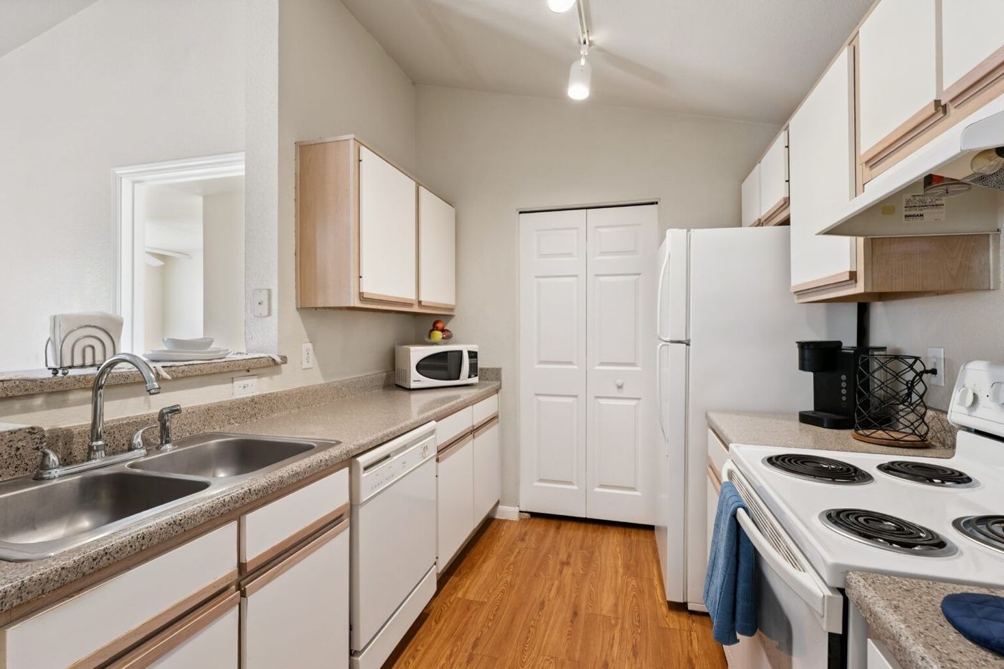 Bright narrow kitchen with white cabinets, wood floor, granite counters, stove, refrigerator, and microwave.