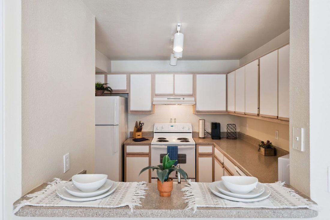 Compact kitchen with white cabinets, beige counters, and a small dining table set for two.