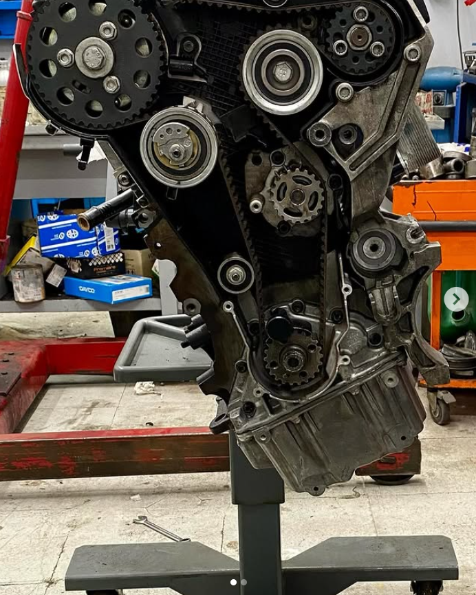Blocco motore su un supporto, che mostra cinghie di distribuzione, pulegge e ingranaggi nell'officina Autoquattro.