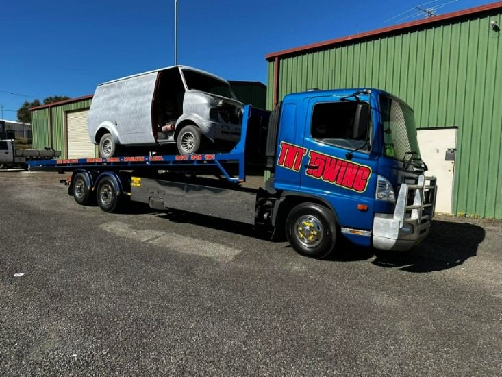 A Blue Tow Truck is Carrying a White Van — TNT Towing - Coffs Clarence in Woolgoolga, NSW