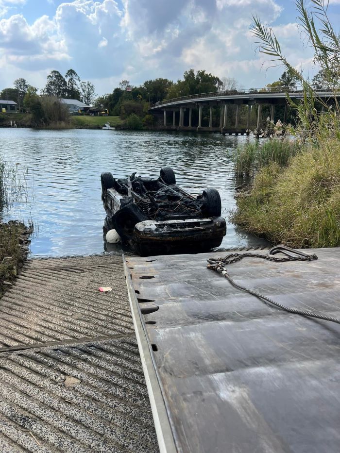 A Car is Sitting on Top of a Trailer Next to a Body of Water — TNT Towing - Coffs Clarence in Coffs Harbour, NSW