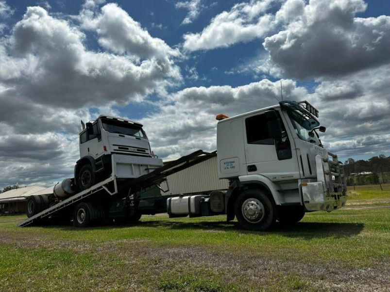 A Tow Truck With a Car on the Back is Parked in a Grassy Field — TNT Towing - Coffs Clarence in Iluka, NSW