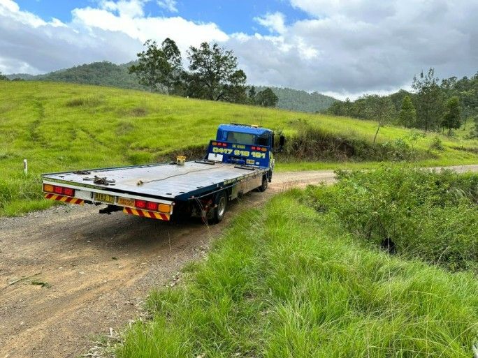 A Blue Tow Truck is Driving Down a Dirt Road — TNT Towing - Coffs Clarence in Lismore, NSW