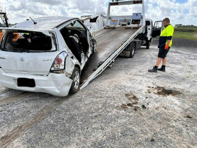 A Man is Standing Next to a Tow Truck With a Damaged Car on It — TNT Towing - Coffs Clarence in South Grafton, NSW