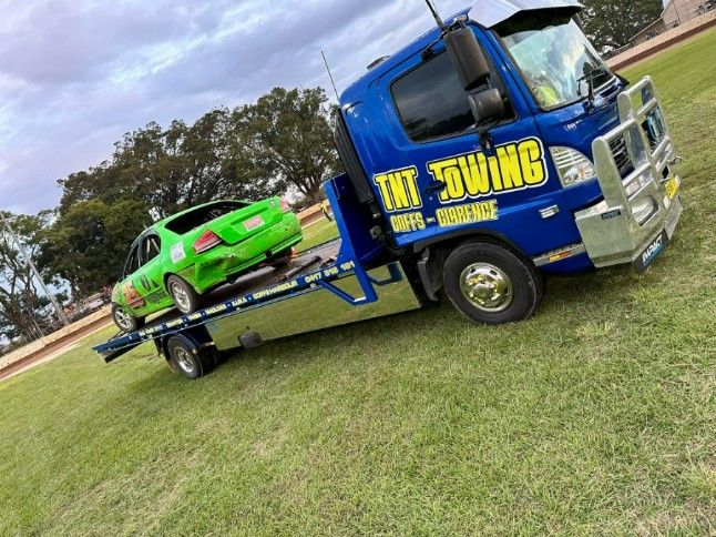 A Blue Tow Truck is Towing a Green Car — TNT Towing - Coffs Clarence in South Grafton, NSW