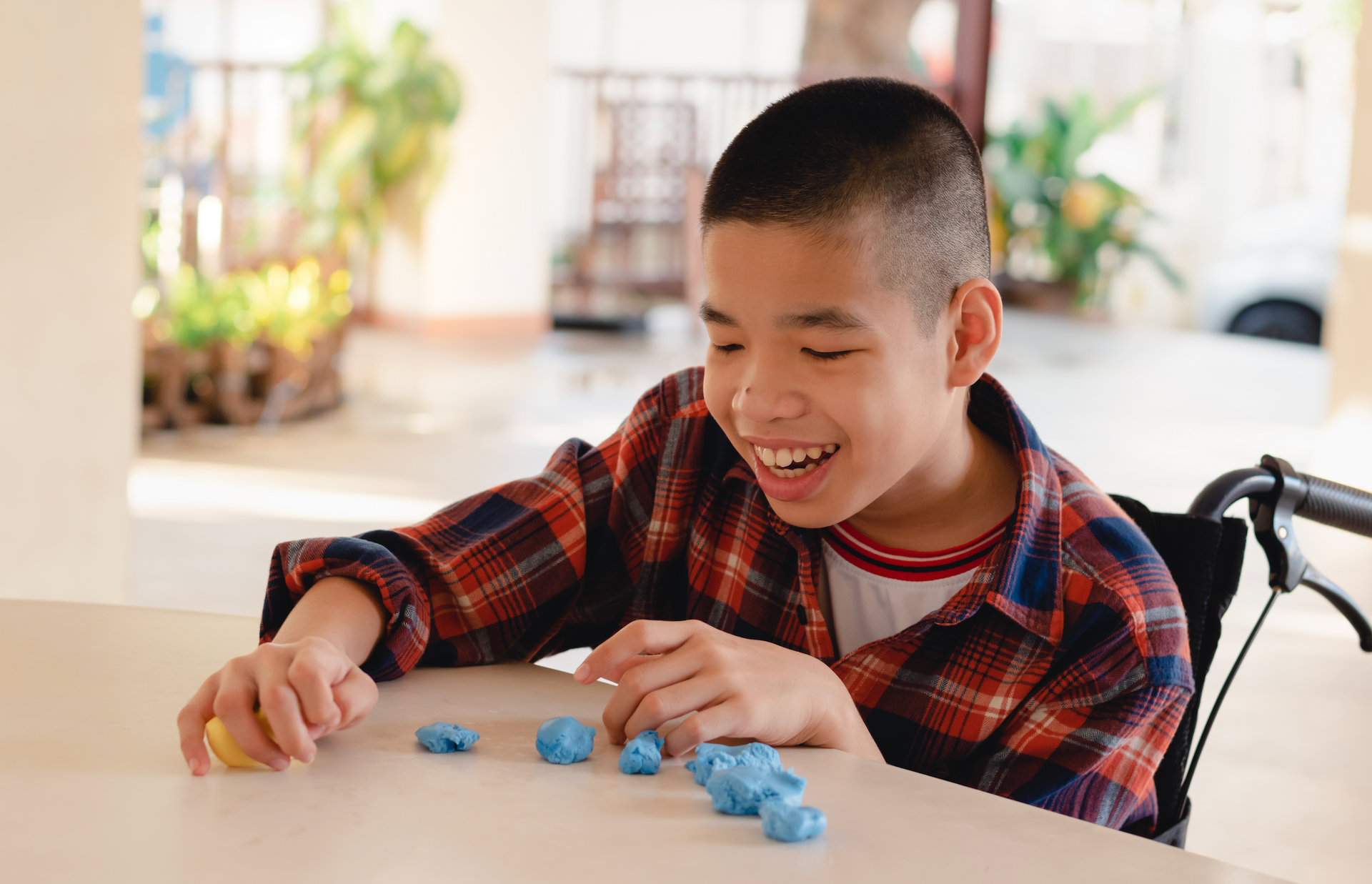 A young boy in a wheelchair is playing with blue play dough.
