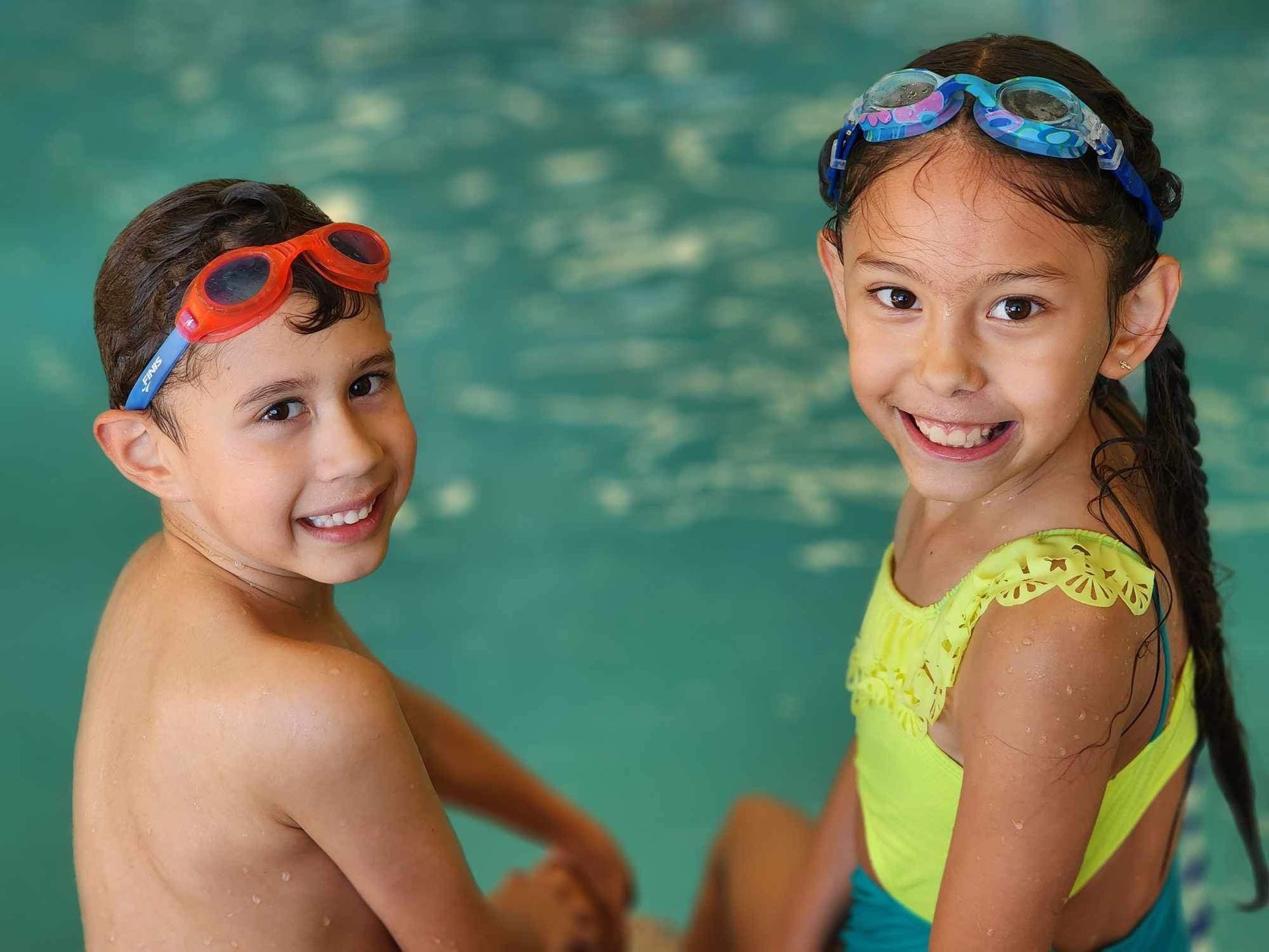 A boy and a girl are sitting next to each other in a swimming pool.