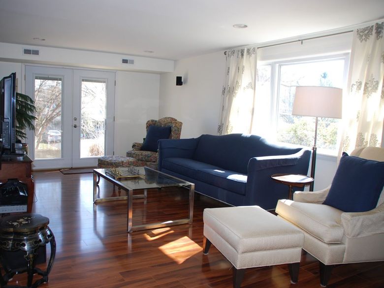 Bright living room with dark blue sofa, white armchair, glass coffee table, and large windows.