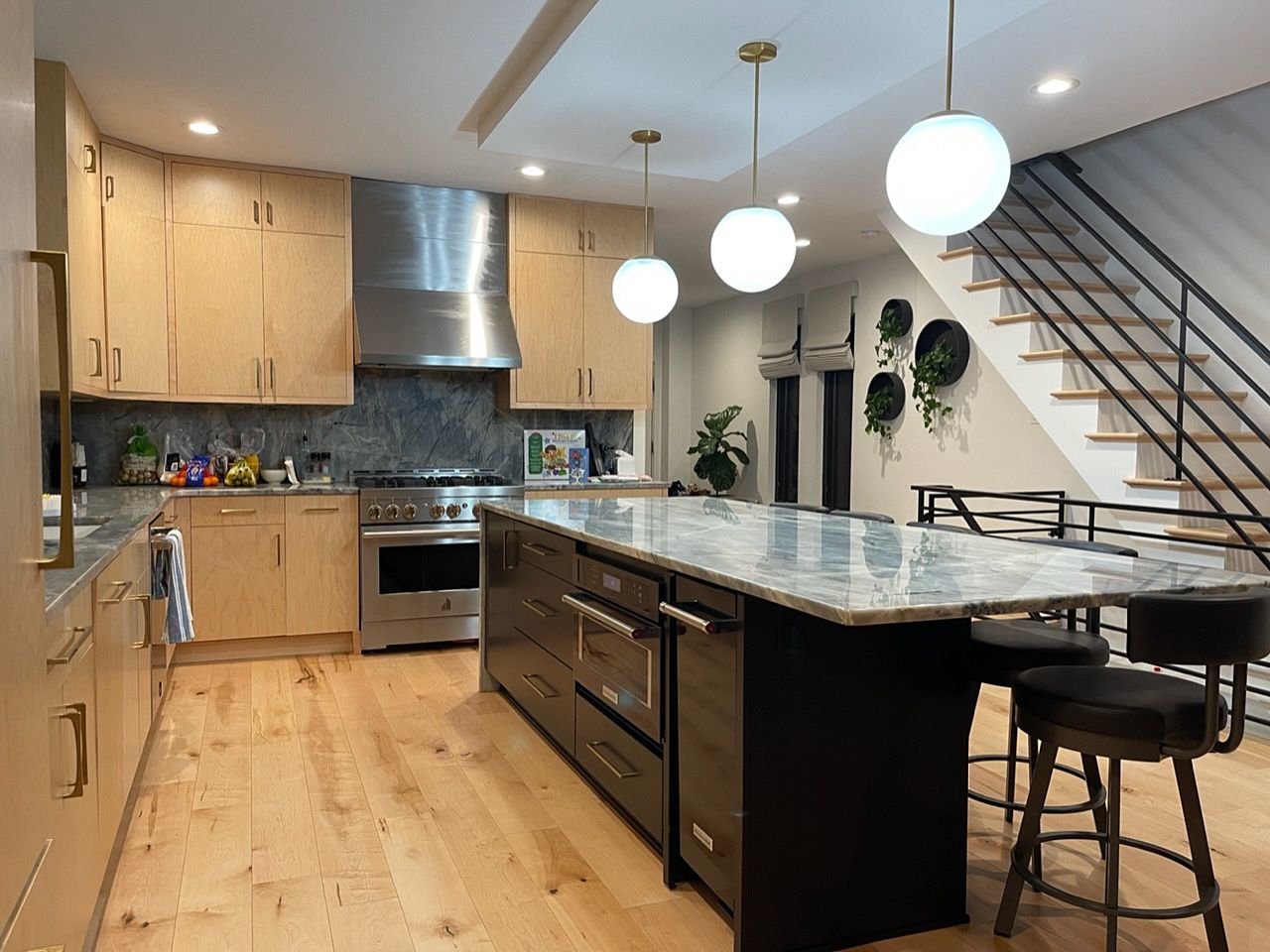 Modern kitchen with marble island, pendant lights, wood cabinets, and staircase in the background