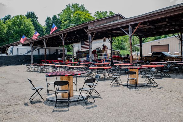 Outdoor patio with red-topped tables, black folding chairs, under a covered structure with American flags.