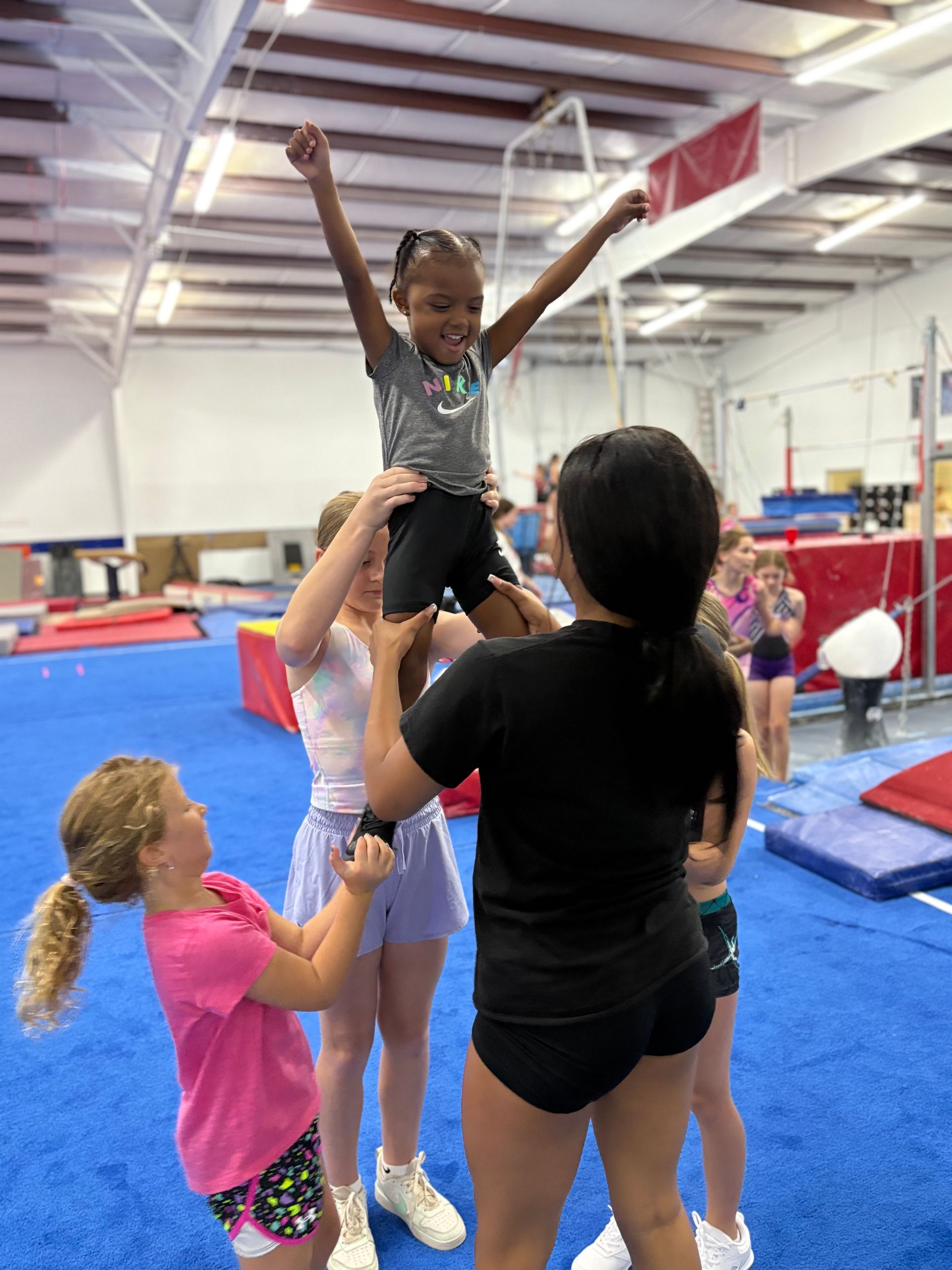 A girl is being lifted in the air by a woman in a gym.