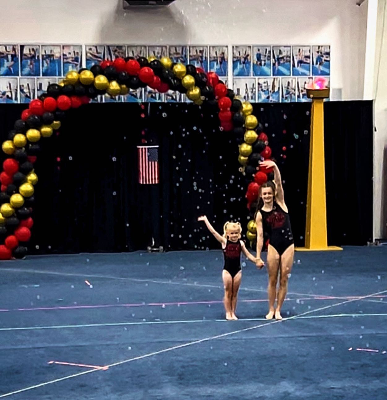 Two girls are standing in front of a balloon arch waving