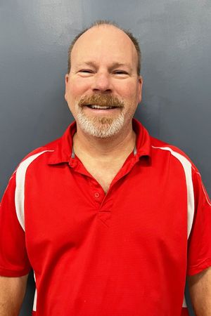 A man with a beard is wearing a red shirt and smiling.