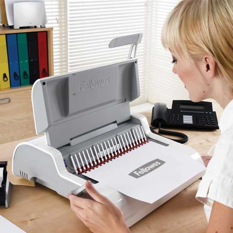 Woman using a white and red comb binding machine on a desk in an office.
