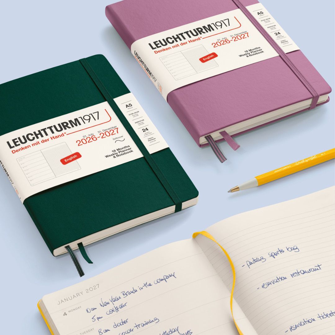 Three Leuchtturm notebooks in green, pink, and cream beside a yellow pencil on a light blue background