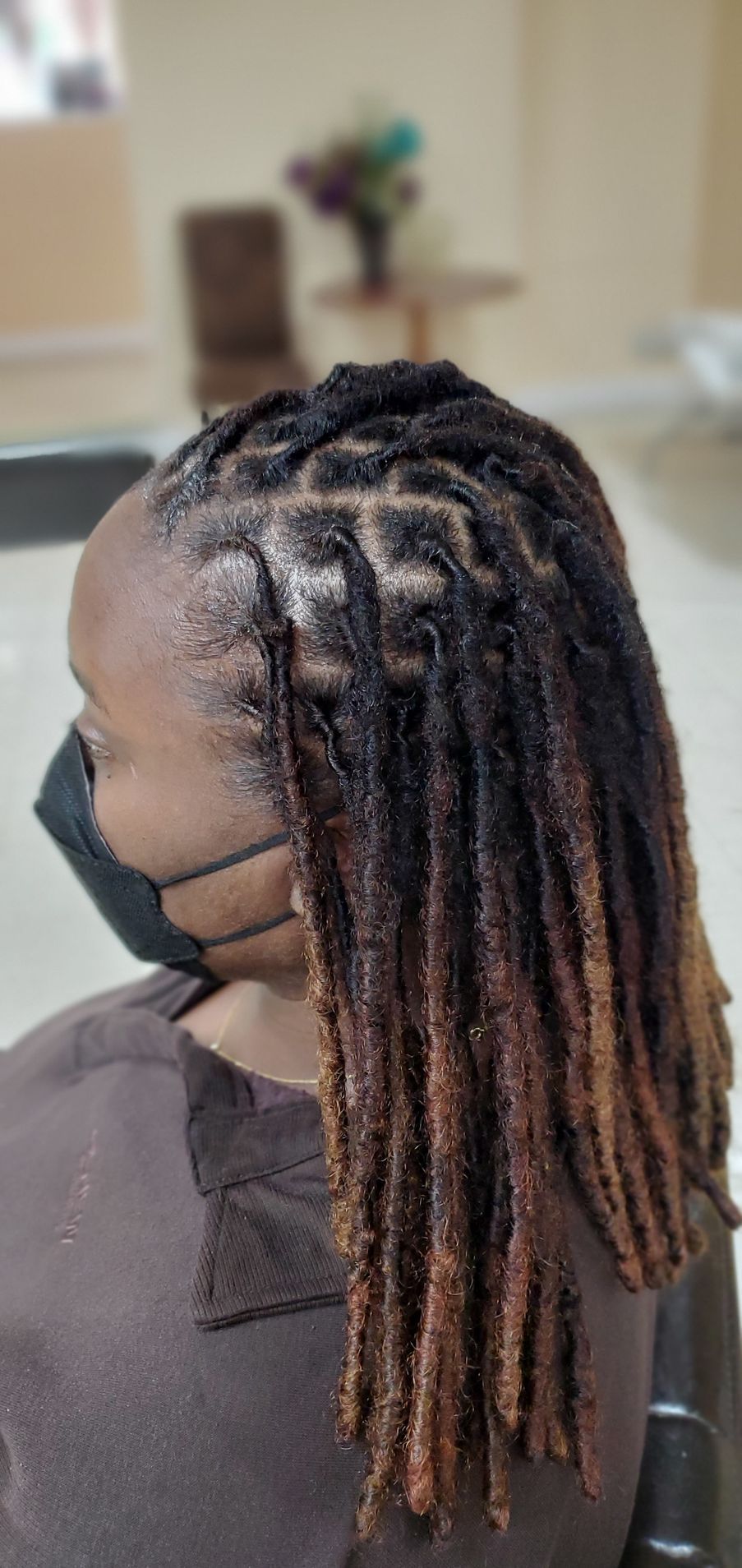 Side view of a person with long braided hair and blond ends, wearing a black face mask.
