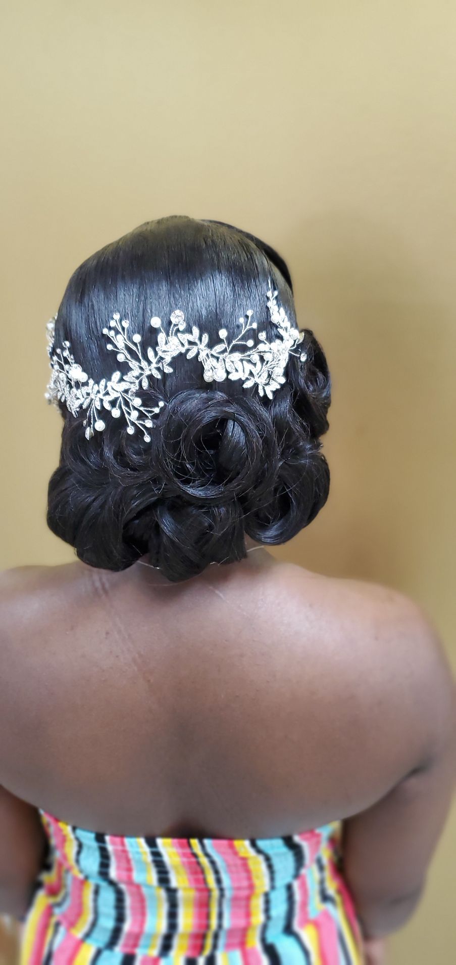 Back view of a woman with a low bun and white floral hair accessory, wearing a striped strapless top.
