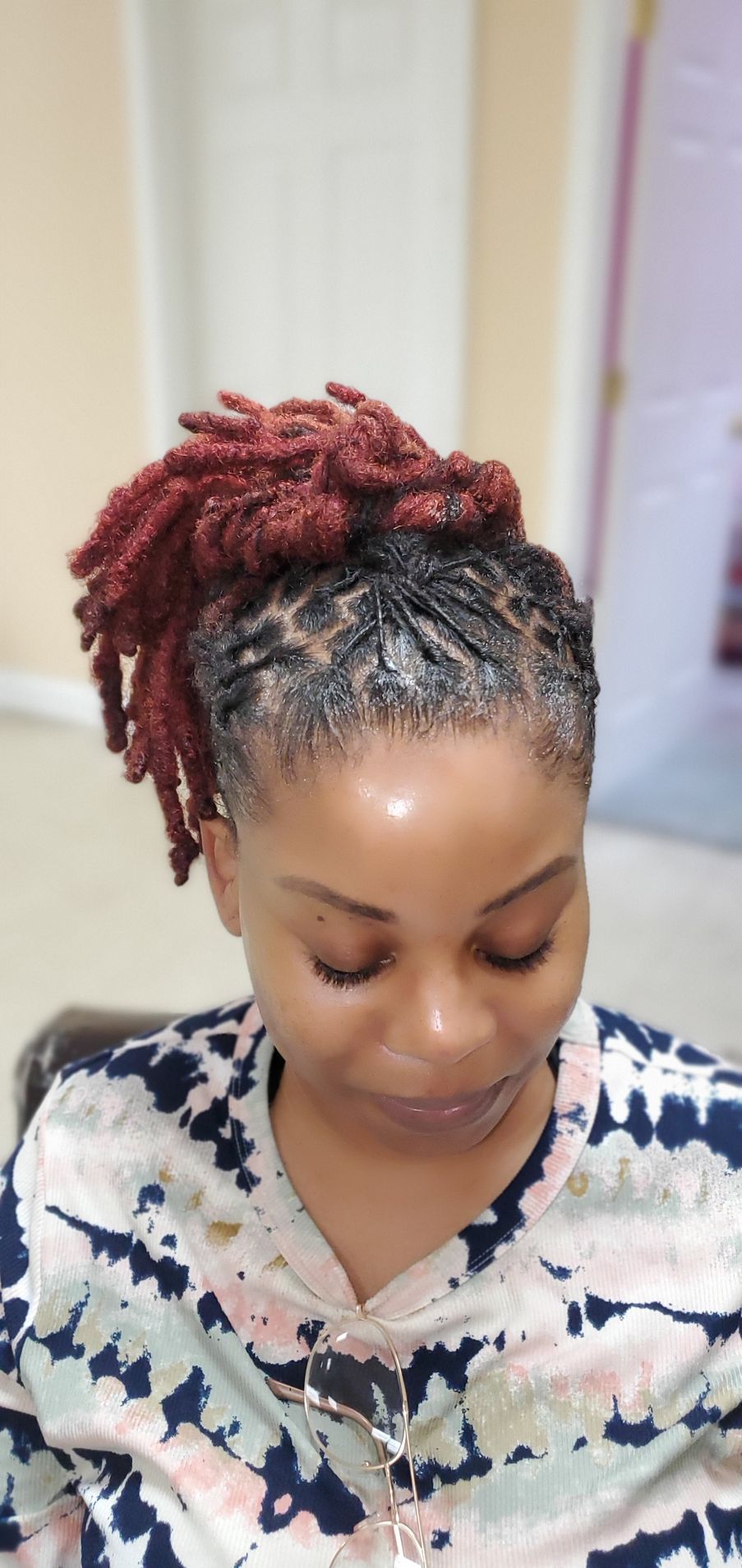 Person with red braided hair looking down, wearing a patterned top indoors