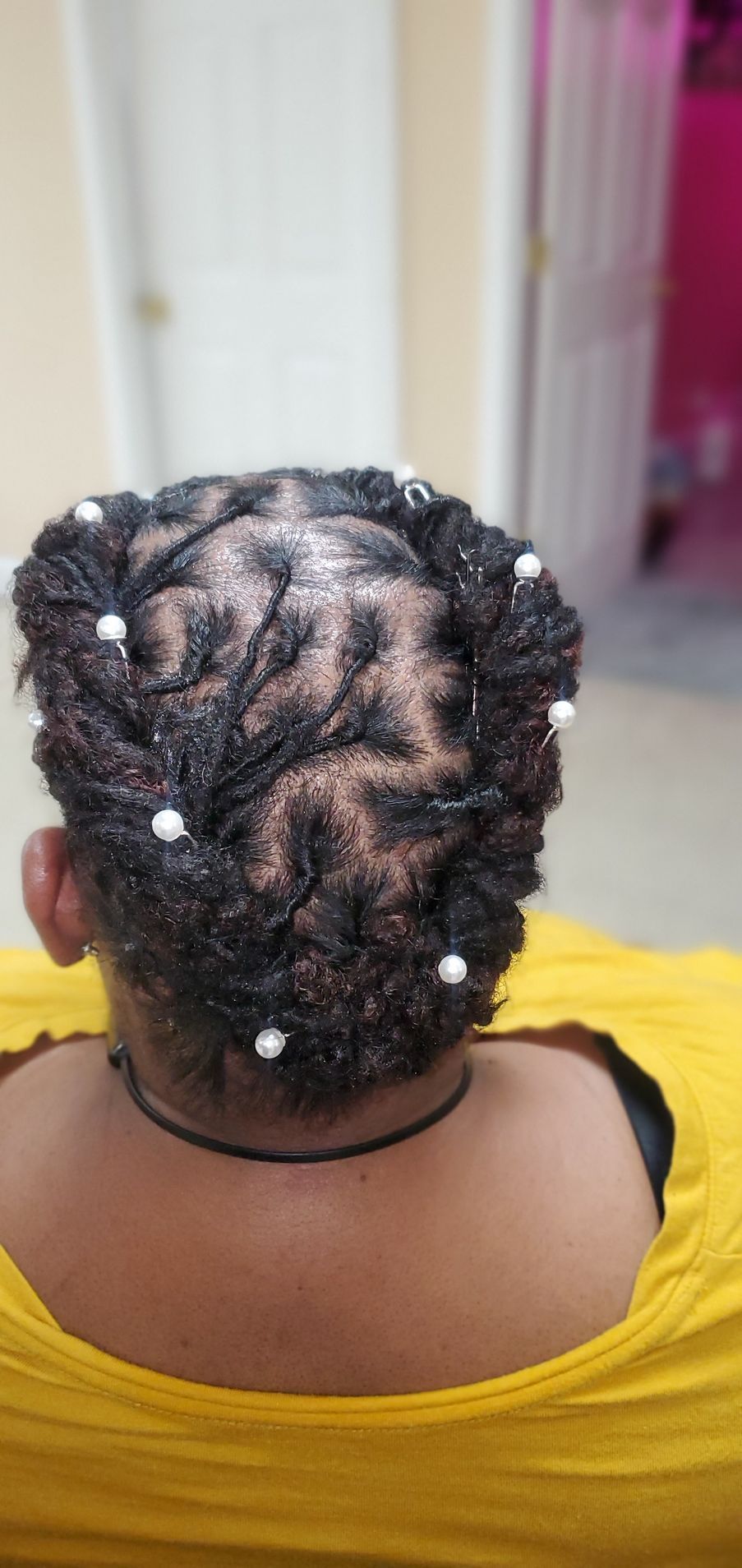 Back of a person with braided hair adorned with white beads, wearing a yellow top indoors