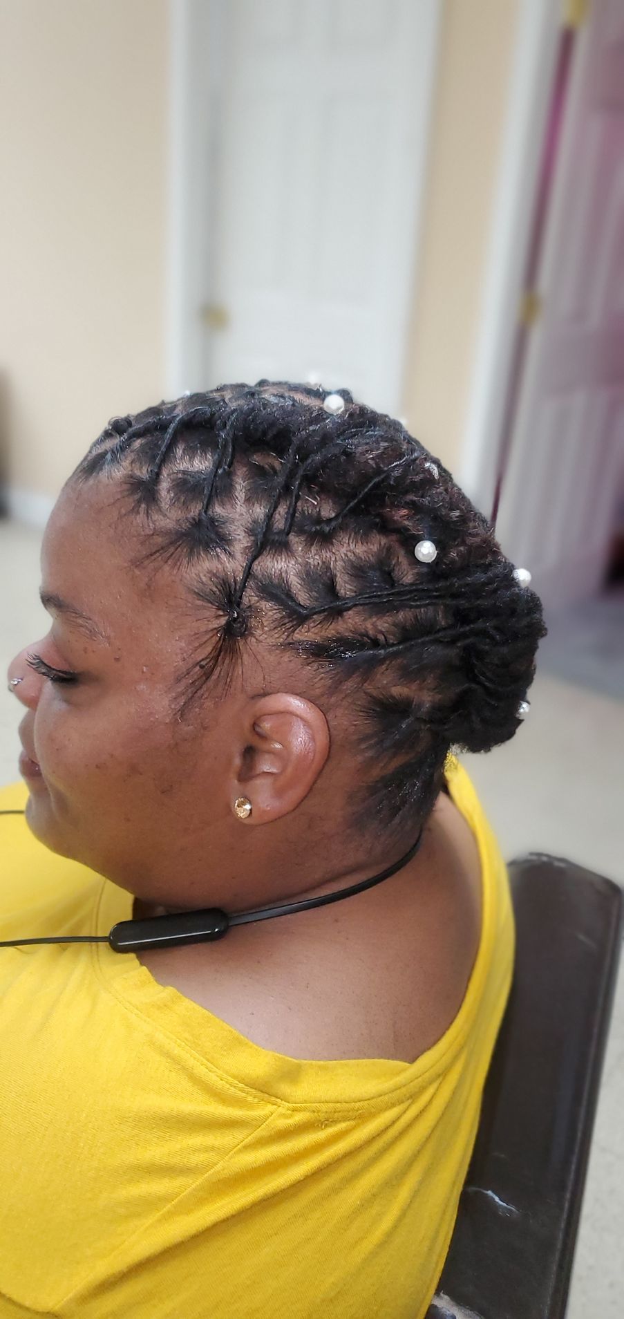 Side view of a person with braided hair wearing a yellow shirt indoors