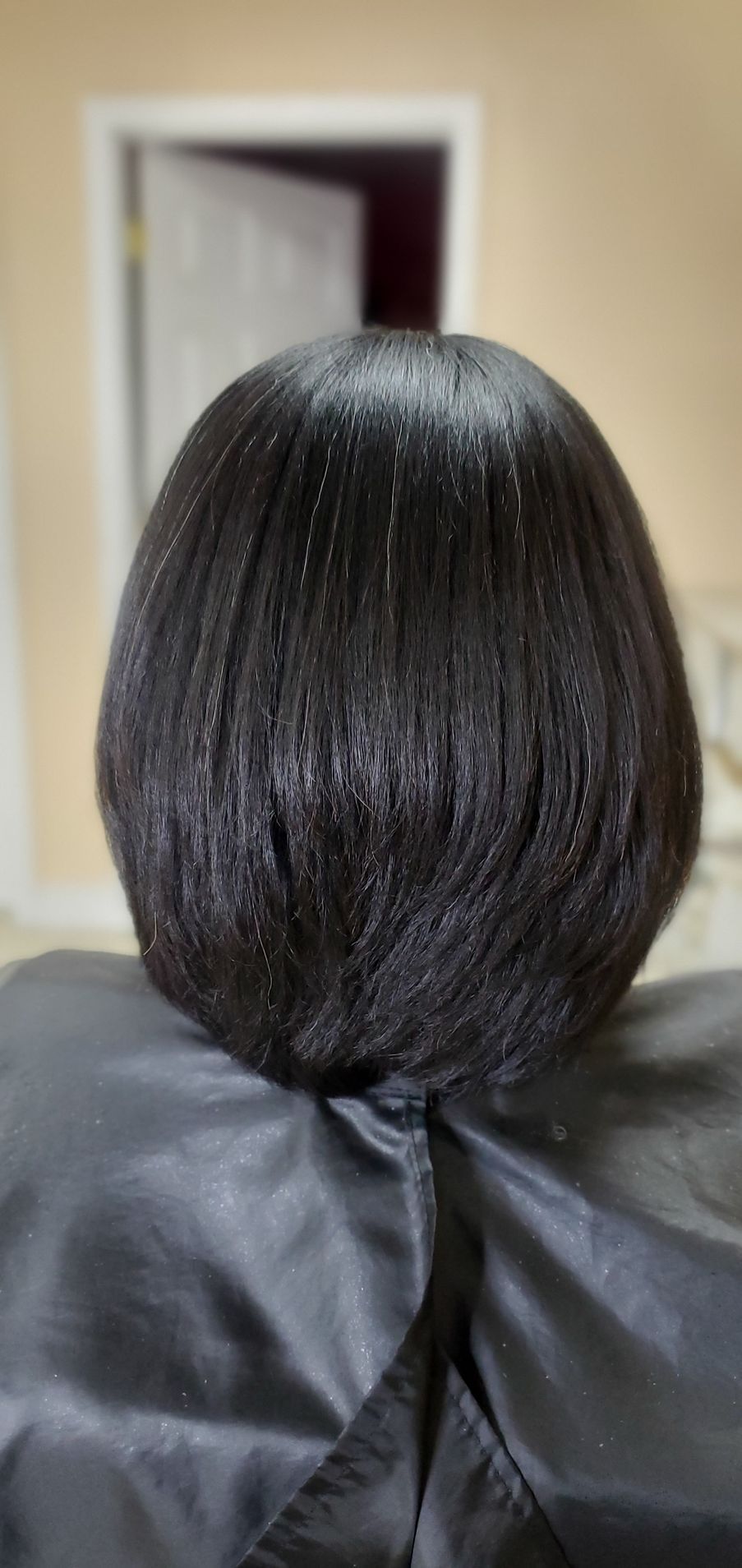 Back view of a sleek black bob haircut with a glossy finish, seated in a salon chair
