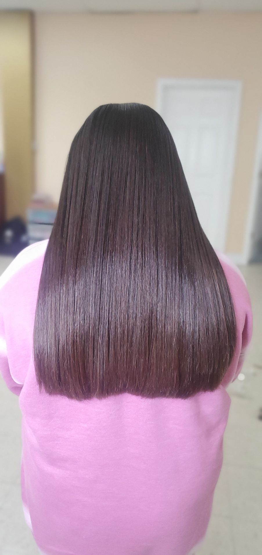 Back view of a person with long dark hair wearing a pink shirt indoors