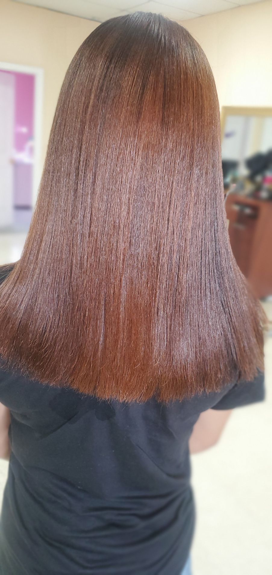 Back view of a person with shoulder-length brown hair in a black shirt indoors